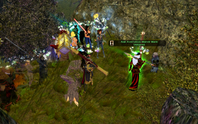 A group of adventurers, including King Alak and Queen Jula of Durakiss, stand at the mouth of a dark, jagged cave entrance. They are engaged in a tense conversation with a gray-skinned druégar deserter, his posture hunched and nervous. The cave looms ominously behind them, its depths shrouded in shadow, while the adventurers' faces are lit by flickering torchlight, revealing expressions of determination and caution.