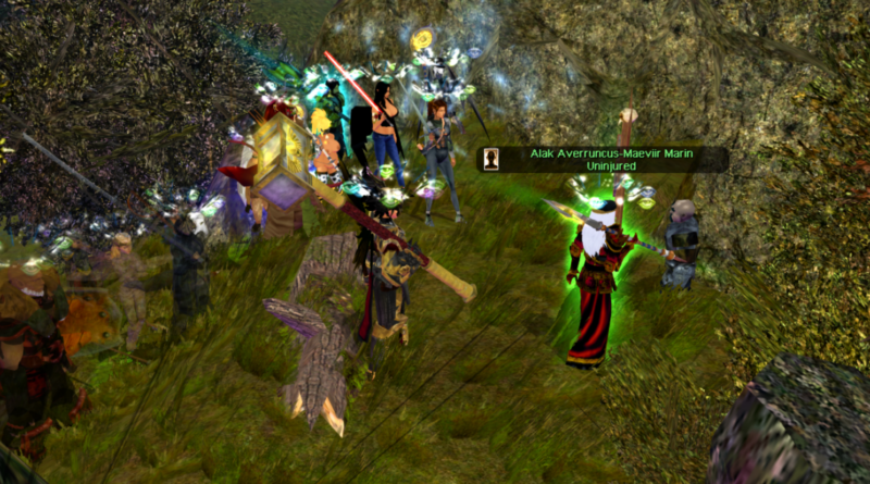 A group of adventurers, including King Alak and Queen Jula of Durakiss, stand at the mouth of a dark, jagged cave entrance. They are engaged in a tense conversation with a gray-skinned druégar deserter, his posture hunched and nervous. The cave looms ominously behind them, its depths shrouded in shadow, while the adventurers' faces are lit by flickering torchlight, revealing expressions of determination and caution.